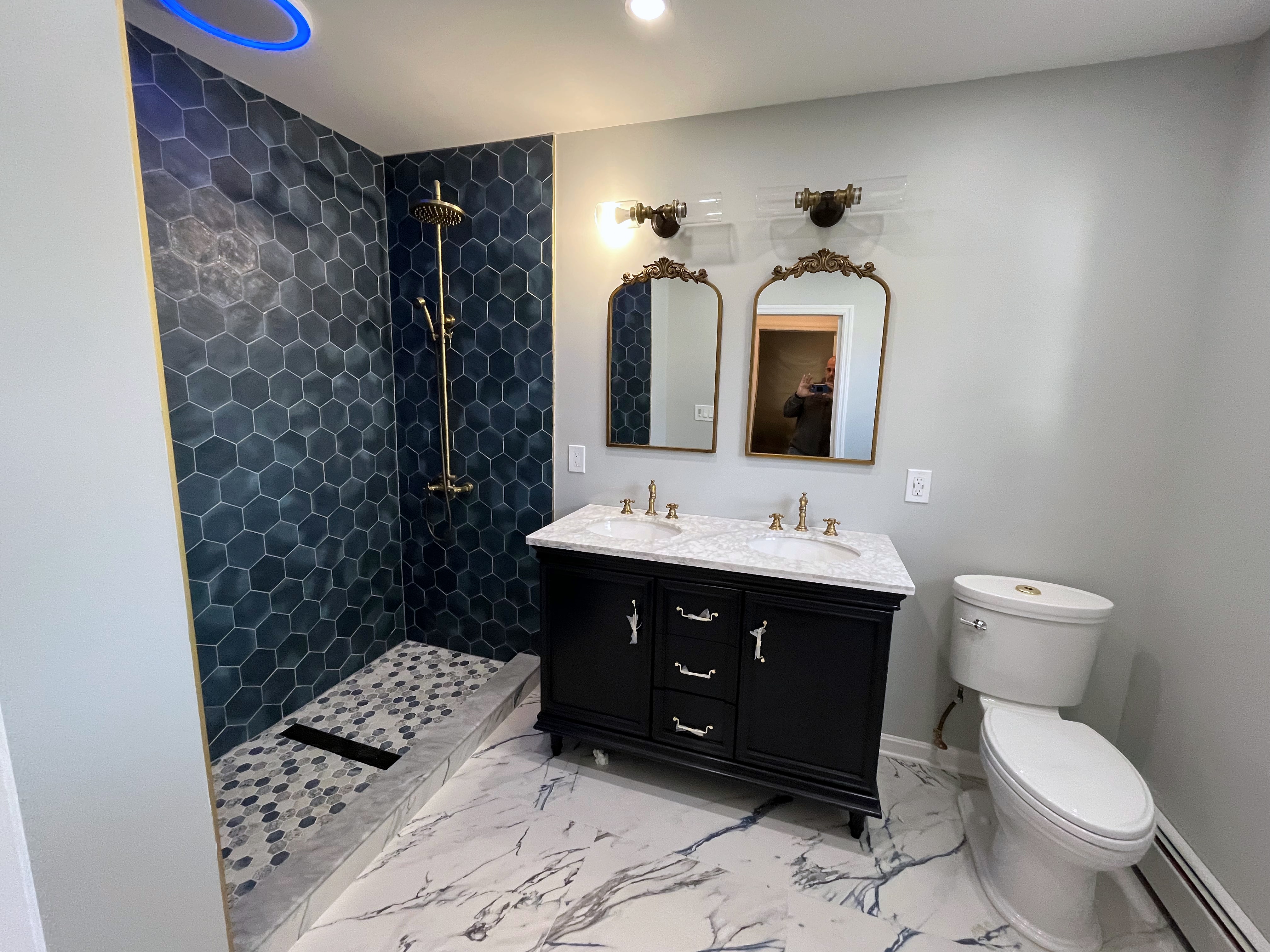 Remodeled bathroom with blue hex-tile shower, black vanity, marble floor